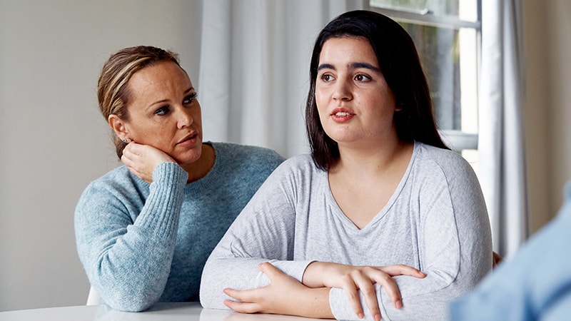 mother and daughter sitting next to each other at table talking